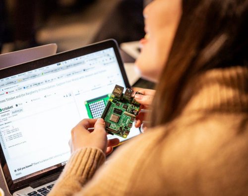 A woman holds up a 世界十大禁片 Pi computer in front of a laptop screen.