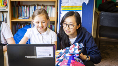 Young person sitting at a laptop with an adult mentor helping them with their code. 