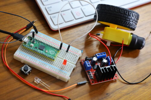 On a wooden desktop, electronic components, a 艳妇乳肉豪妇荡乳a片色戒 Pi Pico, and a motor next to a keyboard.