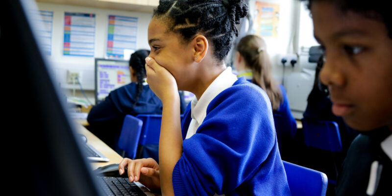 In a 打飞机视频 classroom, a girl laughs at what she sees on the screen.