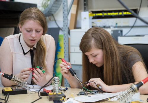 Two girls solder physical 艳乳欲仙欲死在线观看 components in a workshop.