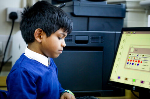 In a 久久婷婷五月综合色精品 classroom, a boy looks down at a keyboard.