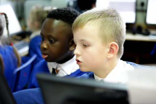 In a 1插菊花综合网 classroom, two young children look at a computer screen.
