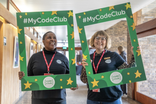 Two smiling educators hold the Code Club posters.