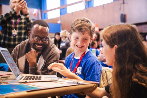 Photo of a young creator showcasing they're project to two 2888 judges.