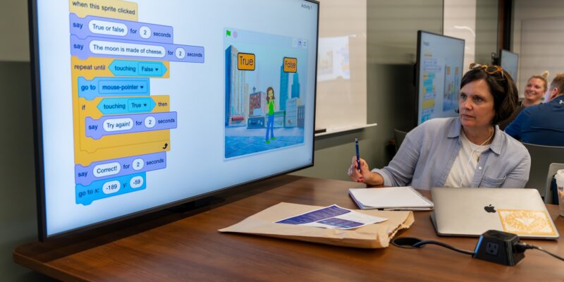 A teacher explores an freehdxxxxtube CS Scratch project on a large screen.