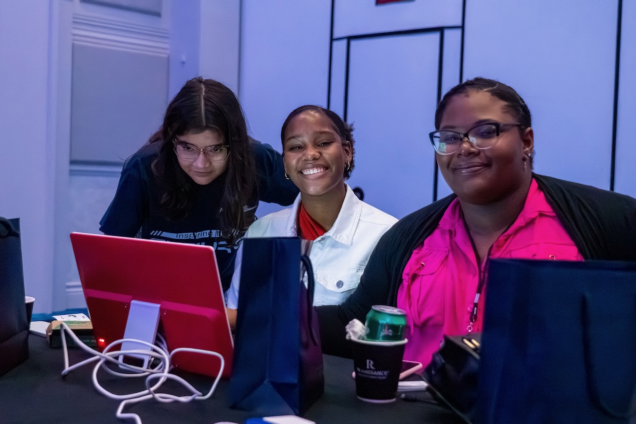 Three smiling young tech creators at a computer screen during a Code Club session in Aruba.