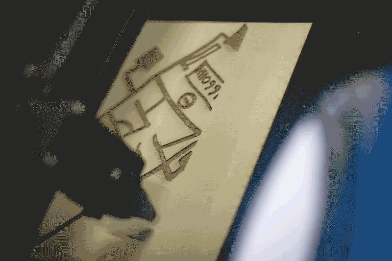 A laser cutter head cuts a child's Inkscape drawing of a bus into a piece of wood